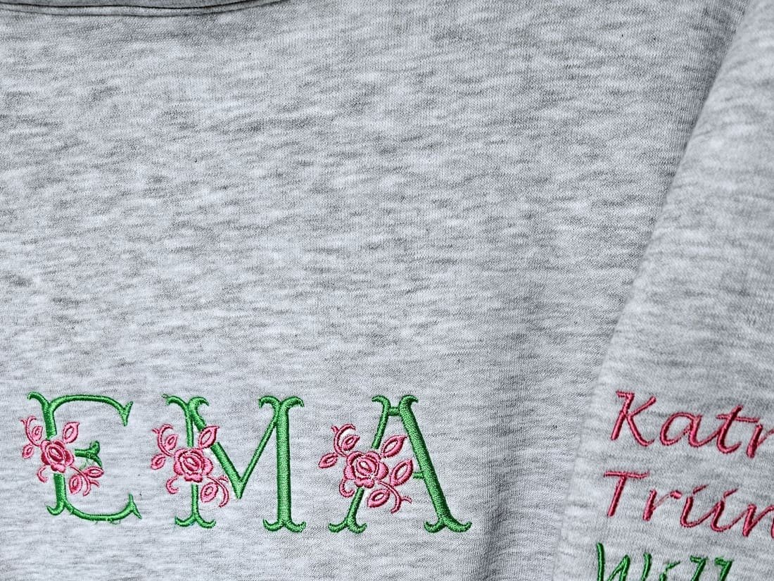 Harmaa collegepaita kirjotulla kukkamonogrammilla ja nimillä hihassa